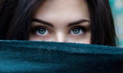 Augentest - Frau mit dunklen langen Haaren blickt hinter einem dunkelblauem Tuch hervor