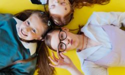Myopie - Drei Mädchen liegen grinsend auf gelben Boden