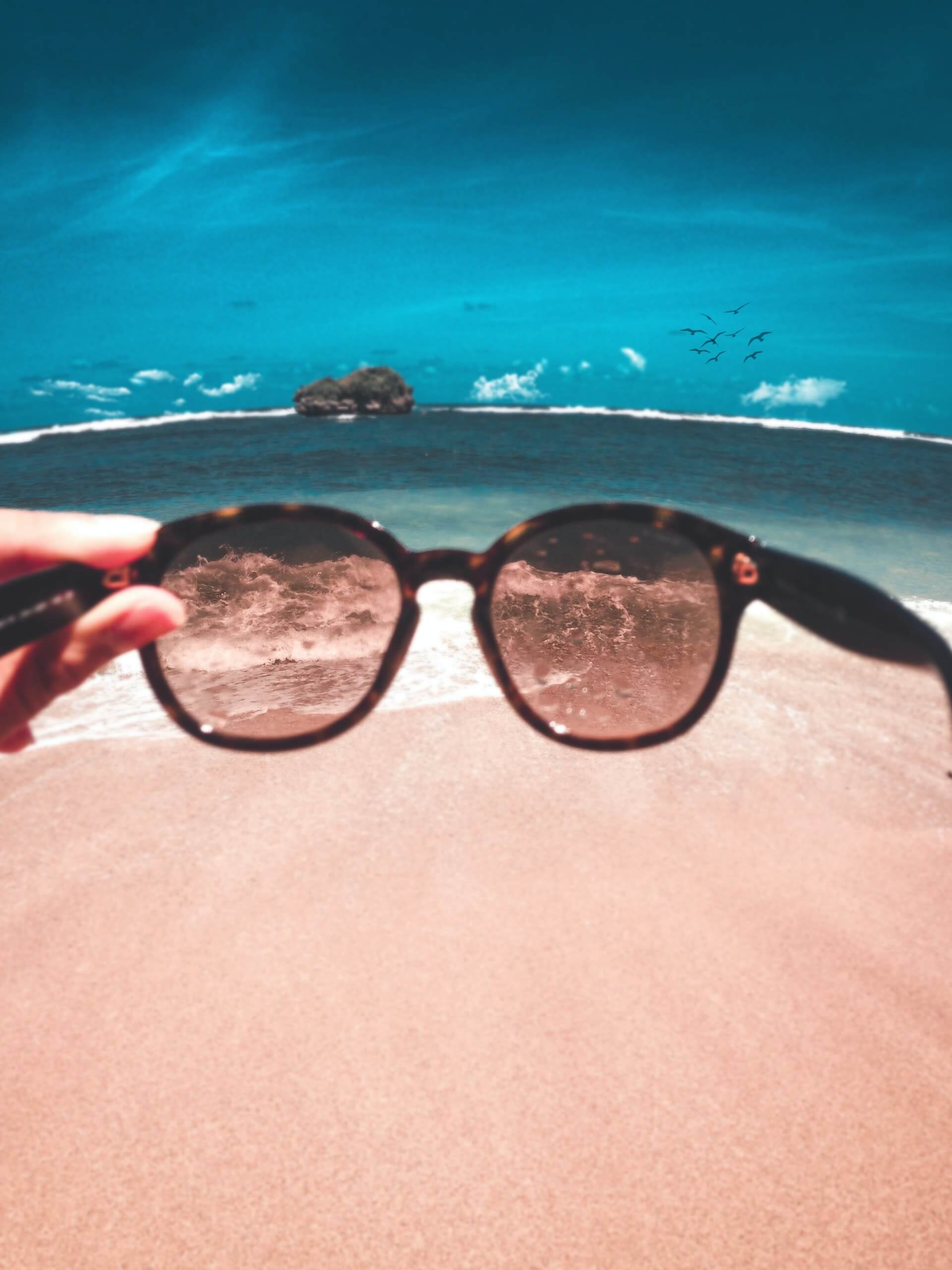 Sonnenbrille, die vor einen Strand gehalten wird - polarisierende Brillengläser