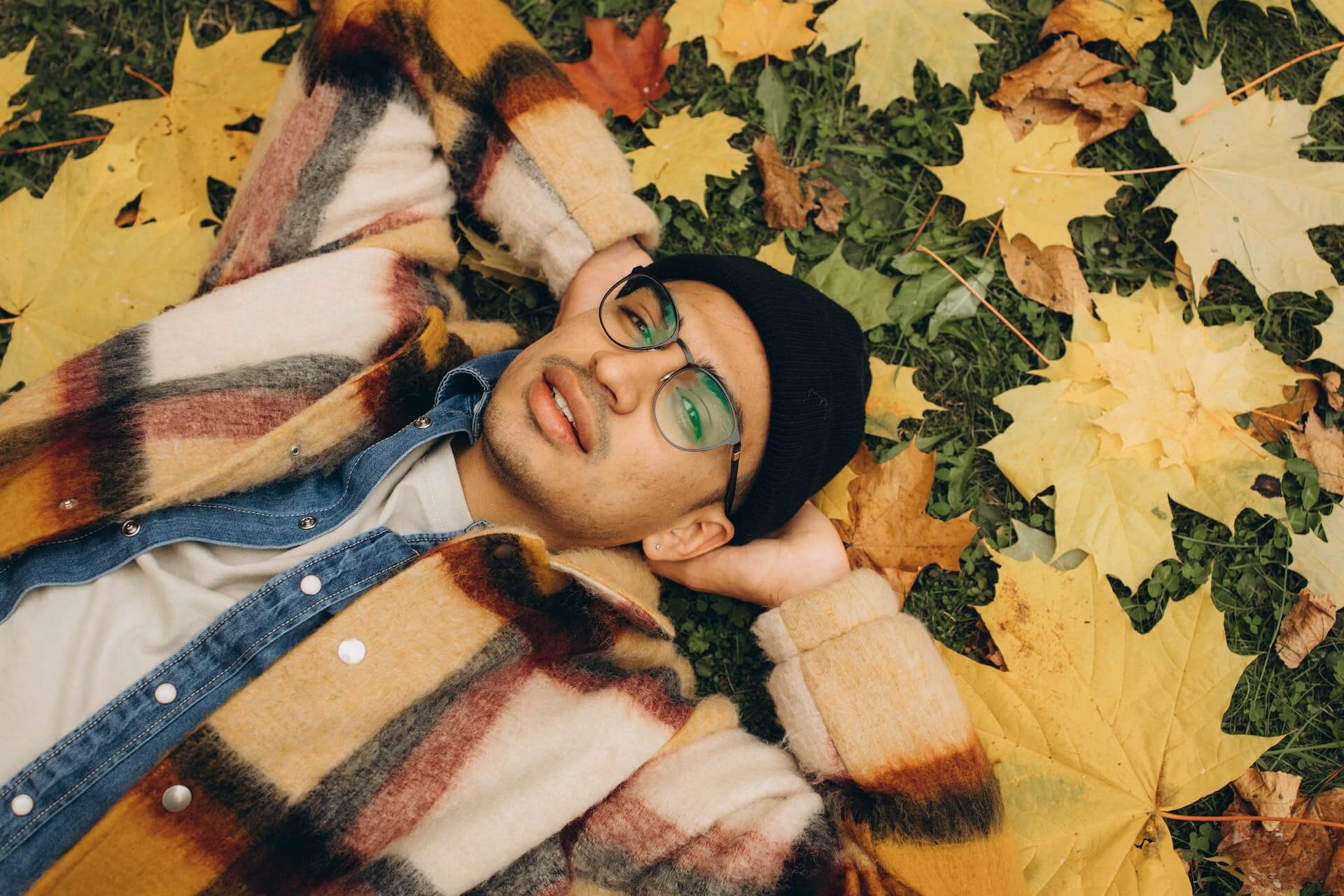 Mann mit Brille liegt auf Wiese mit Herbstblättern