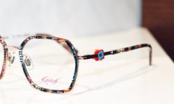 Kaos-Bille mit Detail auf Brillenbügel. Ein rotes und hellblaues Quadrat liegen übereinander