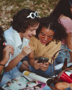 Gruppe von jungen Frauen mit Sonnenbrillen, die auf ein Handy schauen, dient als Illustration für den Artikel: Ray Ban-Sonnenbrillen?