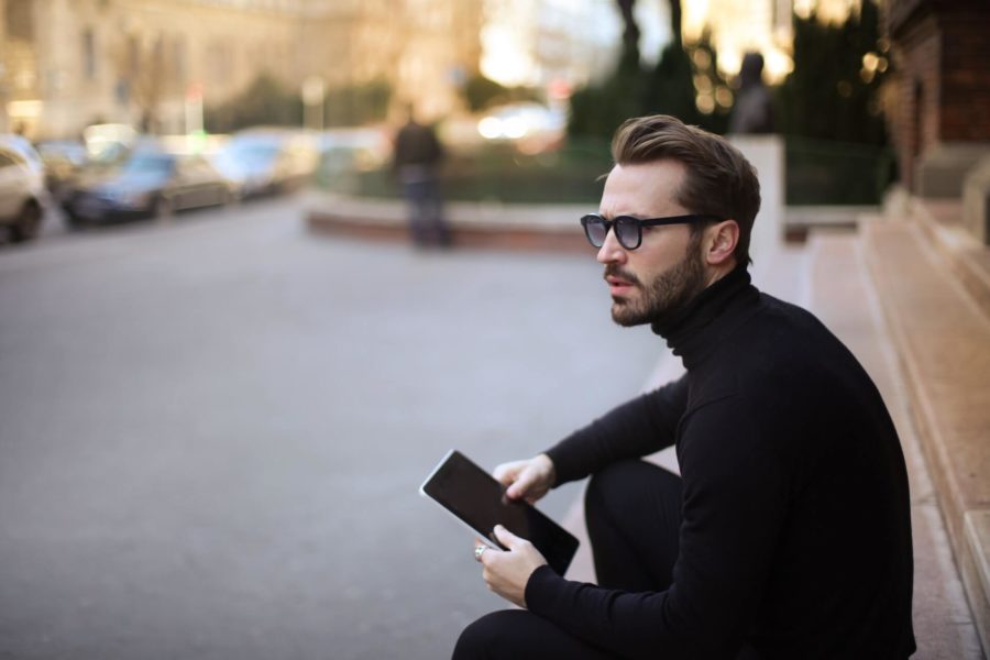 Sitzender Mann mit  Brille und einem Tablet in der Hand.