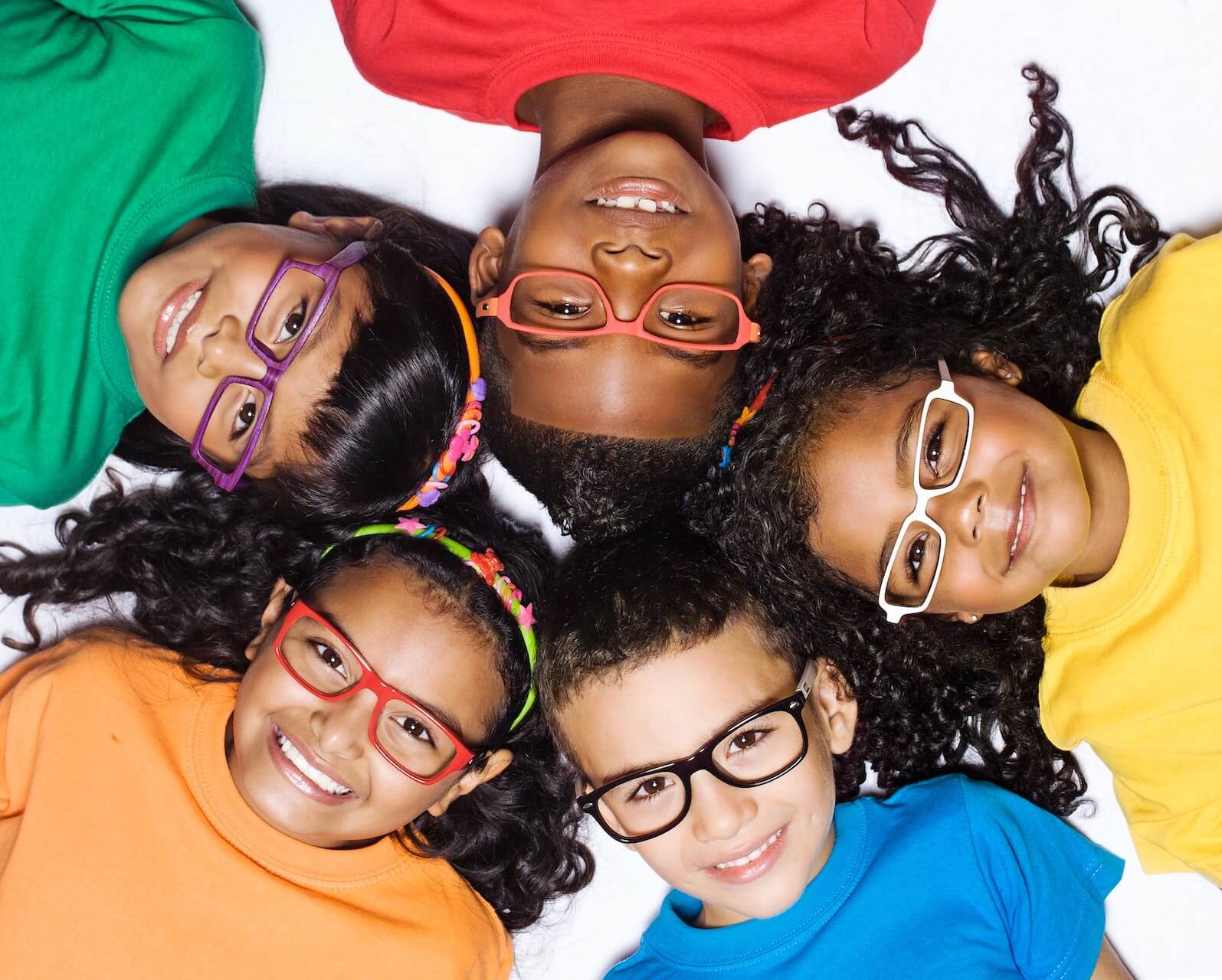 Fünf Kinder mit Brillen, die sternförmig auf dem Boden liegen