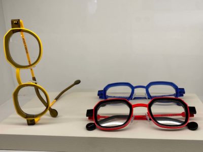 Drei Brillen mit schwarzen Rahmen und Farbakzenten je Brille in gelb, rot und blau von Brillenmanufaktur Anne & Valentin- Brillentrends 2024