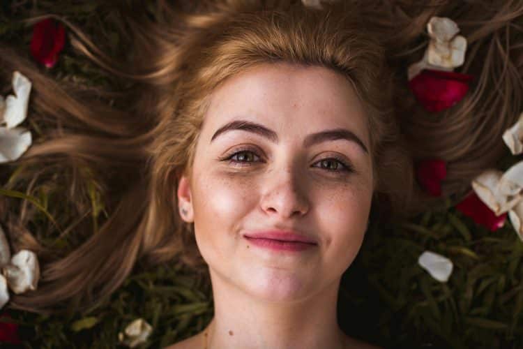 Gesicht einer grinsende Frau, die auf einer Blumenwiese liegt