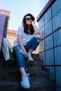 Junge Frau, die mit einer Sonnenbrille auf der Nase auf einer Treppe sitzt