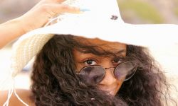 Frau mit Sonnenbrille, die ihren Hut festhält