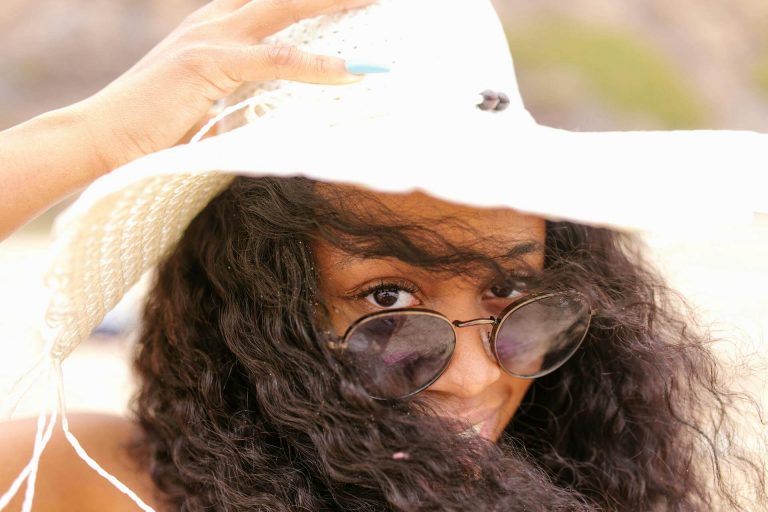 Frau mit Sonnenbrille, die ihren Hut festhält