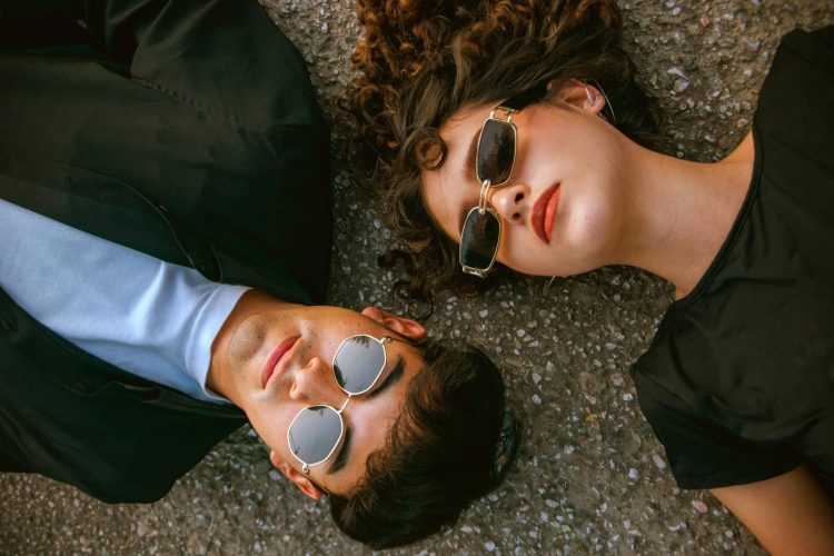 Photo by César O'neill Ein junger Mann und eine junge Frau tragen Sonnenbrillen und liegen auf dem Boden